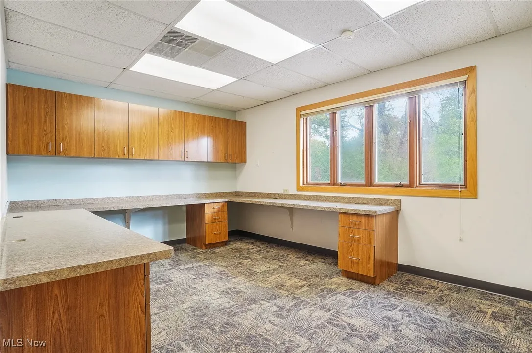 Unfurnished office featuring built in desk and a drop ceiling