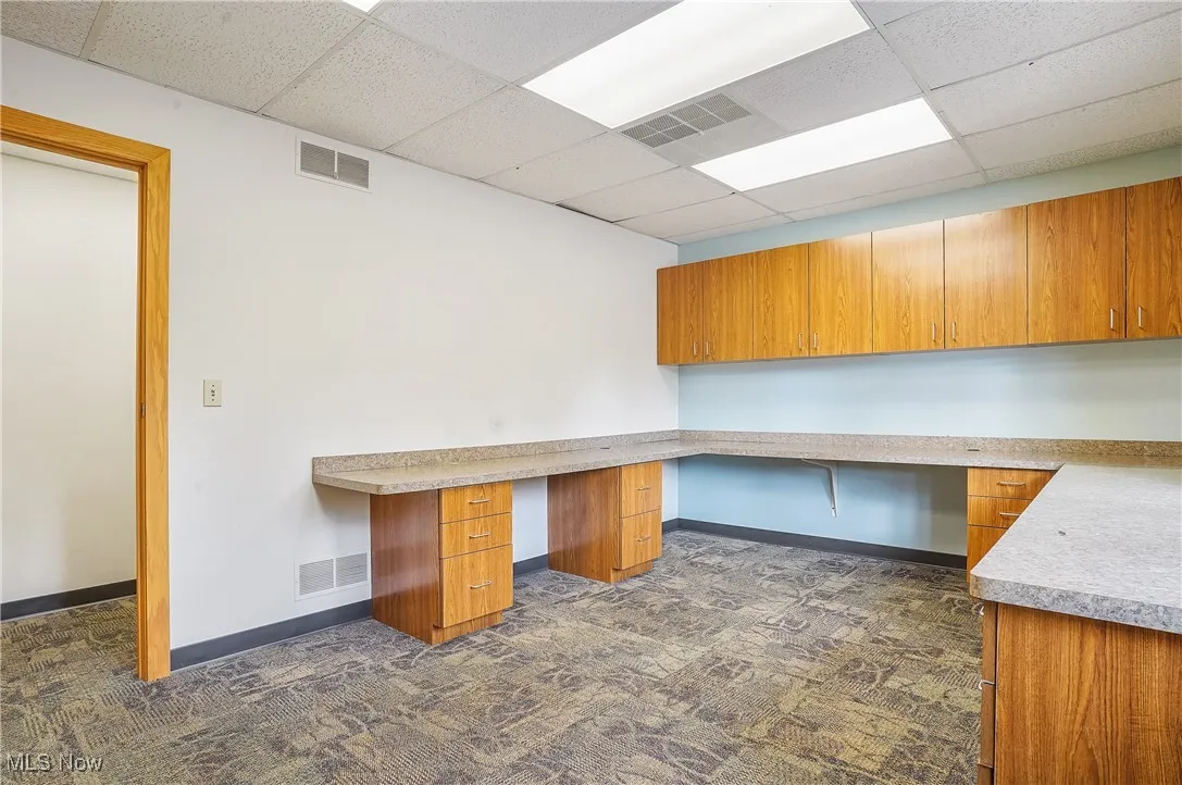 Unfurnished office with built in desk, a drop ceiling, and dark colored carpet