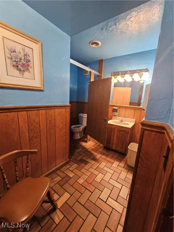 Bathroom featuring a shower with door, vanity, wooden walls, and toilet