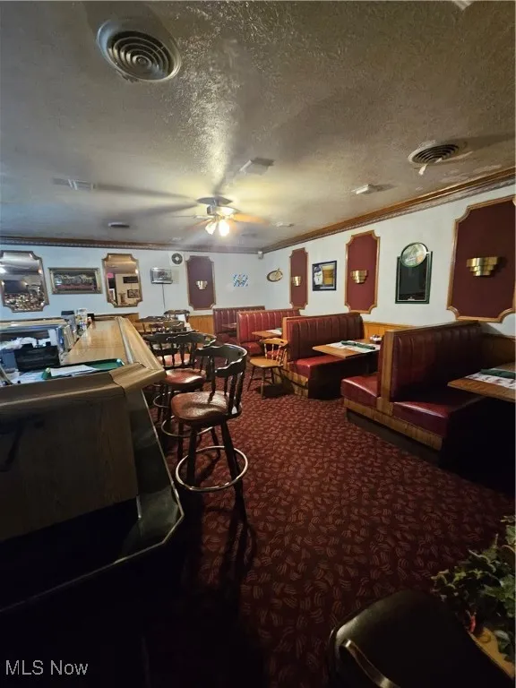 Rec room with carpet flooring, a textured ceiling, ornamental molding, and ceiling fan
