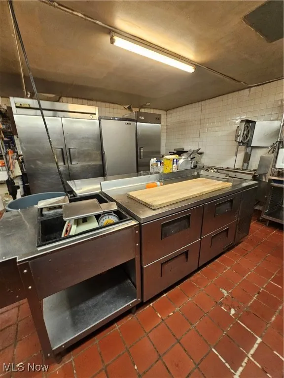 Kitchen with fridge, dark tile patterned floors, stainless steel counters, and backsplash