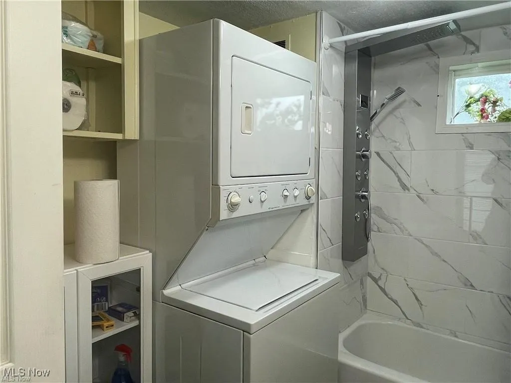 Clothes washing area with a textured ceiling and stacked washer and dryer