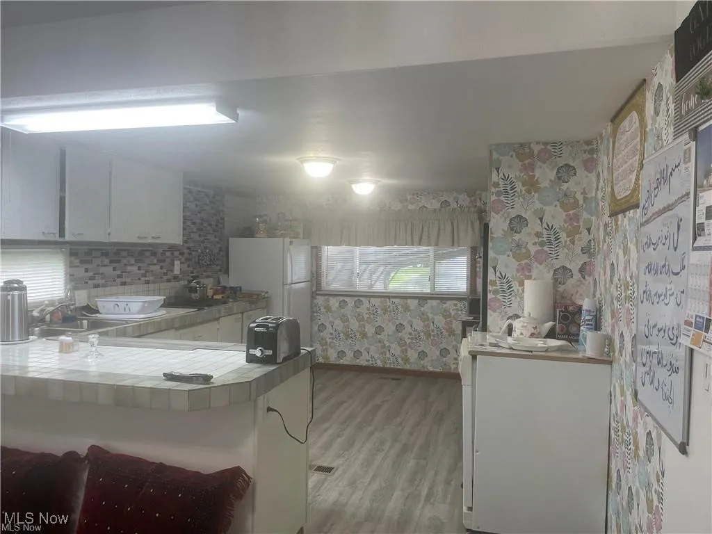 Kitchen with sink, light wood-type flooring, tile countertops, white cabinetry, and white fridge