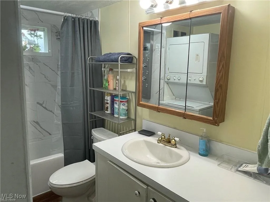 Full bathroom with vanity, stacked washer / drying machine, shower / bath combo with shower curtain, and toilet