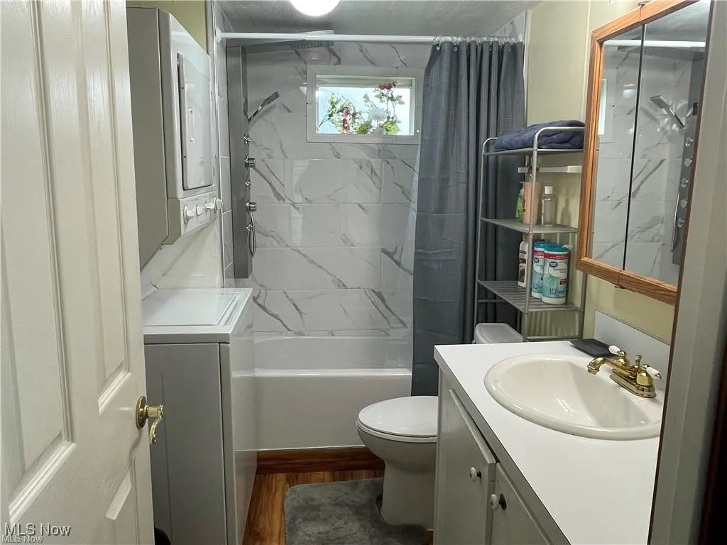 Full bathroom featuring wood-type flooring, shower / tub combo with curtain, toilet, vanity, and stacked washer / drying machine