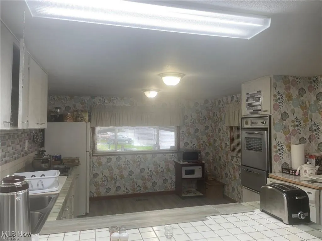 Kitchen with white cabinets, tile counters, light hardwood / wood-style floors, and oven