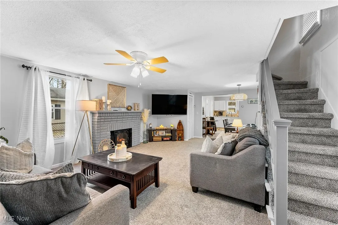 Living room featuring a textured ceiling, a fireplace, carpet flooring, and ceiling fan