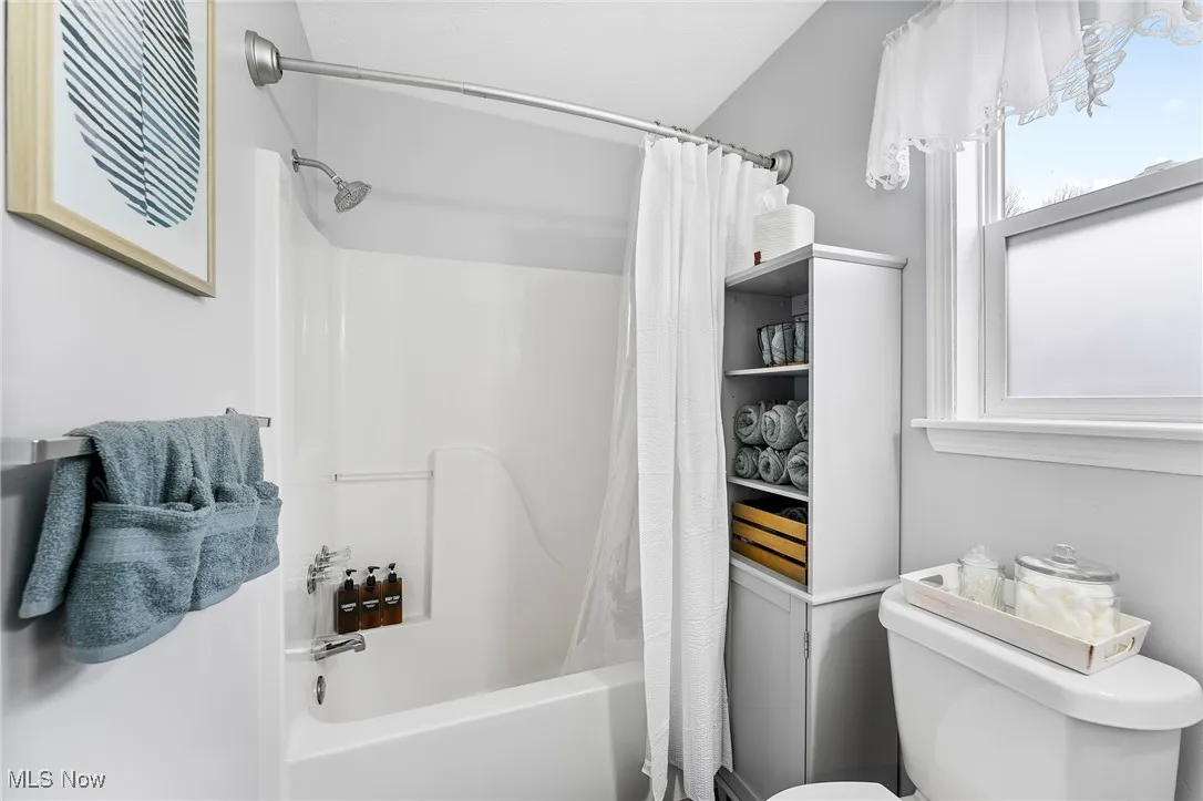 Bathroom featuring toilet and shower / bathtub combination with curtain