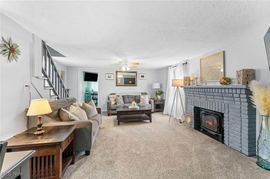 Living room with a textured ceiling, carpet flooring, a fireplace, and ceiling fan
