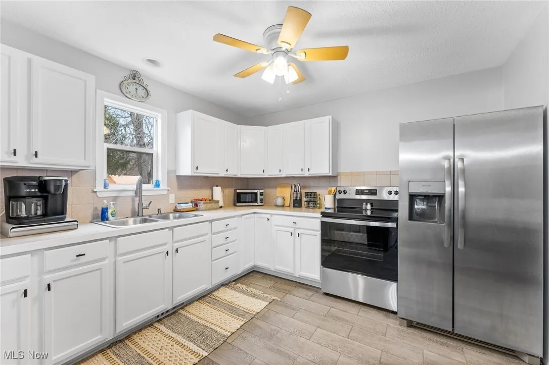 Kitchen featuring sink, appliances with stainless steel finishes, white cabinetry, and ceiling fan