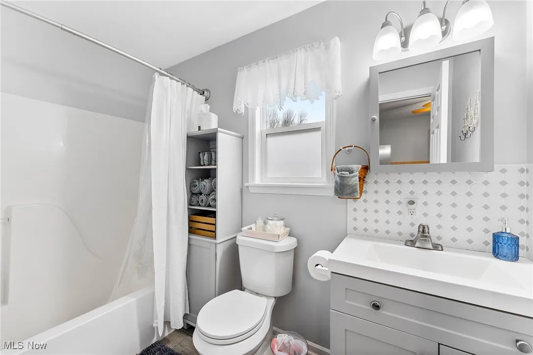 Full bathroom featuring backsplash, vanity, toilet, and shower / bathtub combination with curtain