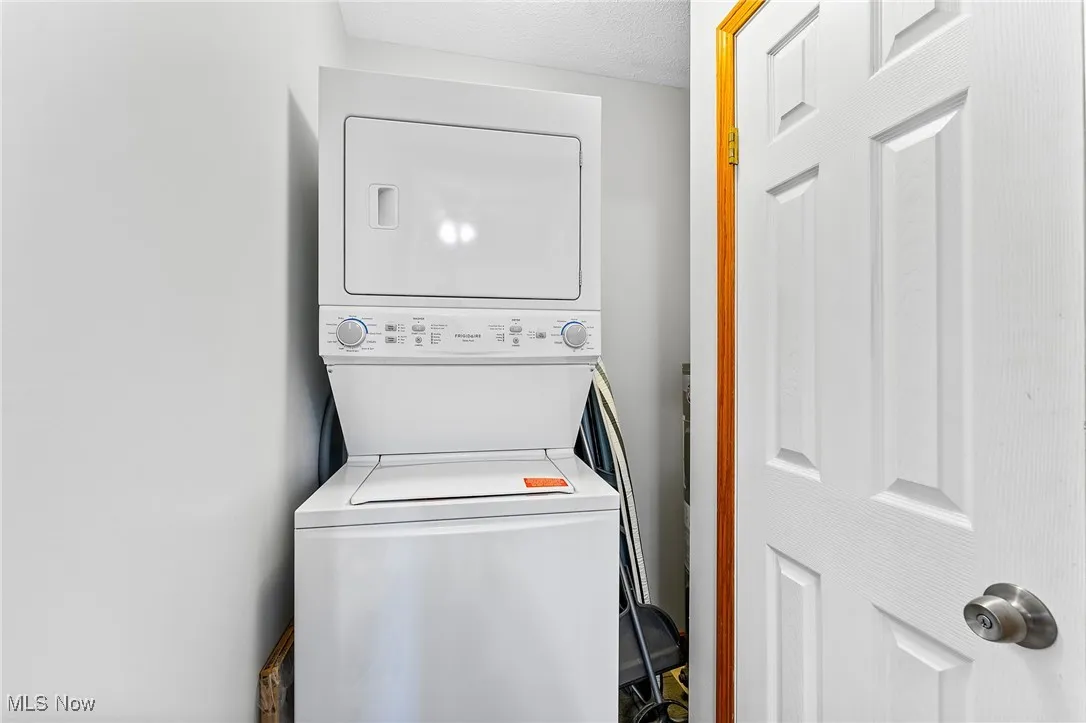 Clothes washing area with a textured ceiling and stacked washer / dryer