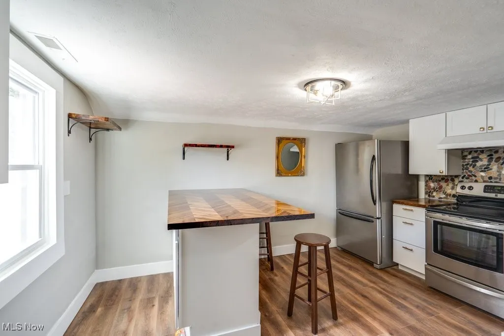 Kitchen with white cabinets, a kitchen breakfast bar, premium range hood, wooden counters, and stainless steel appliances