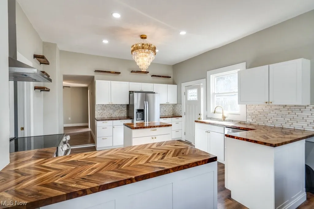 Kitchen featuring wall chimney range hood, stainless steel fridge, white cabinets, sink, and a center​​‌​​​​‌​​‌‌​‌‌​​​‌‌​‌​‌​‌​​​‌​​ island