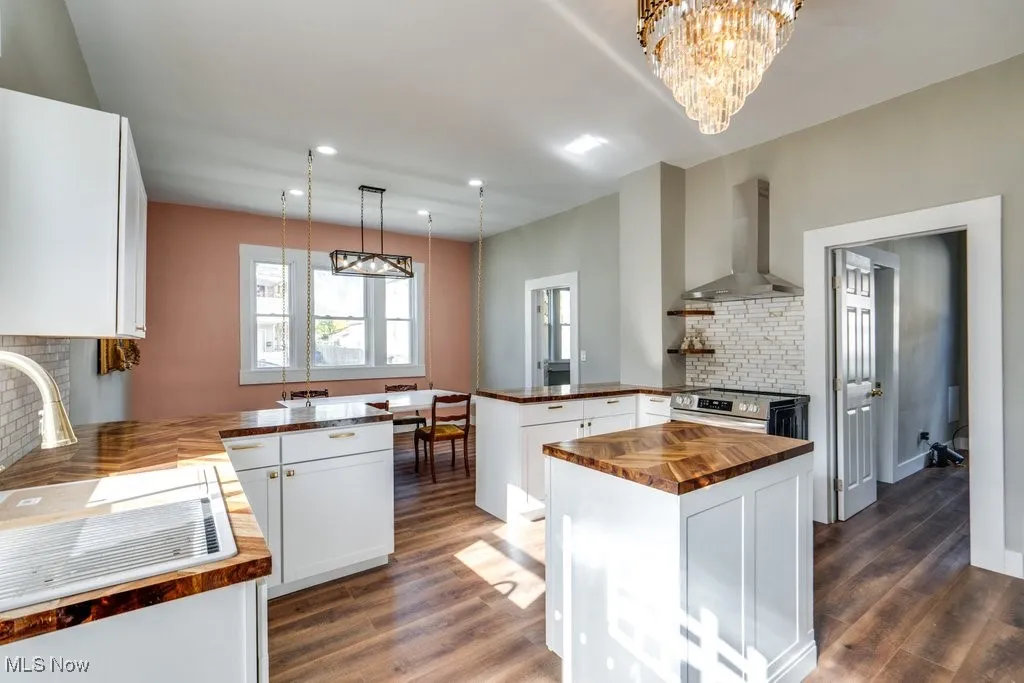 Kitchen with decorative backsplash, wall chimney range hood, kitchen peninsula, a center island, and electric stove