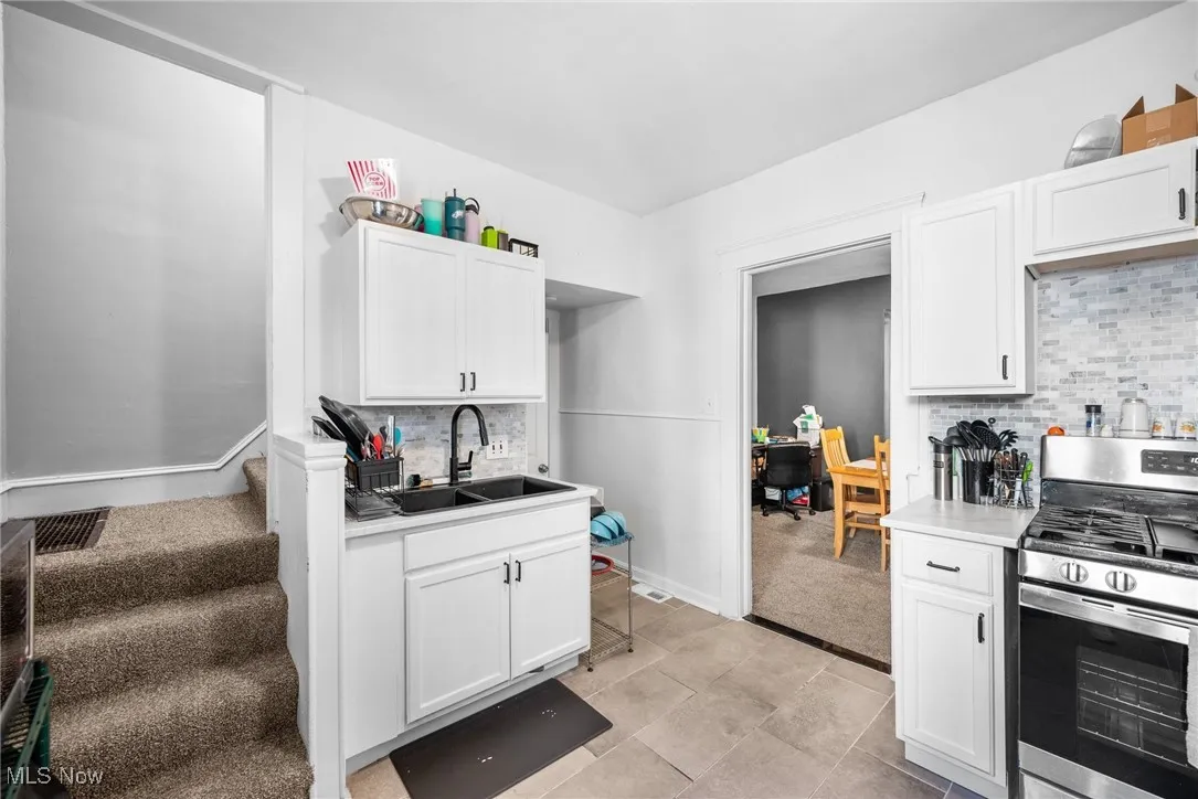 Kitchen featuring tasteful backsplash, sink, white cabinetry, stainless steel stove, and light colored carpet
