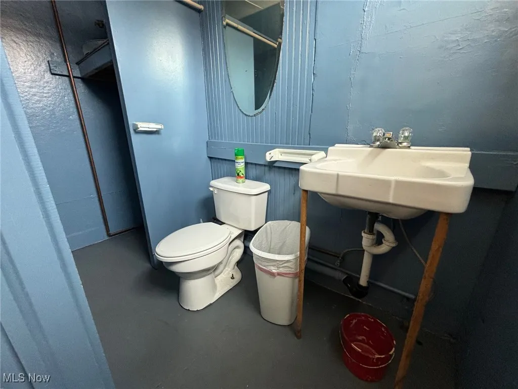 Bathroom with toilet, concrete flooring, and sink