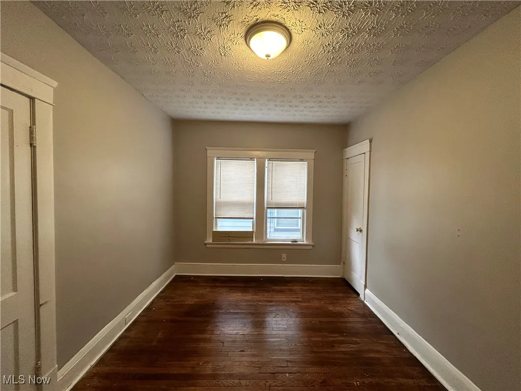 Unfurnished room featuring dark wood-type flooring and a textured ceiling