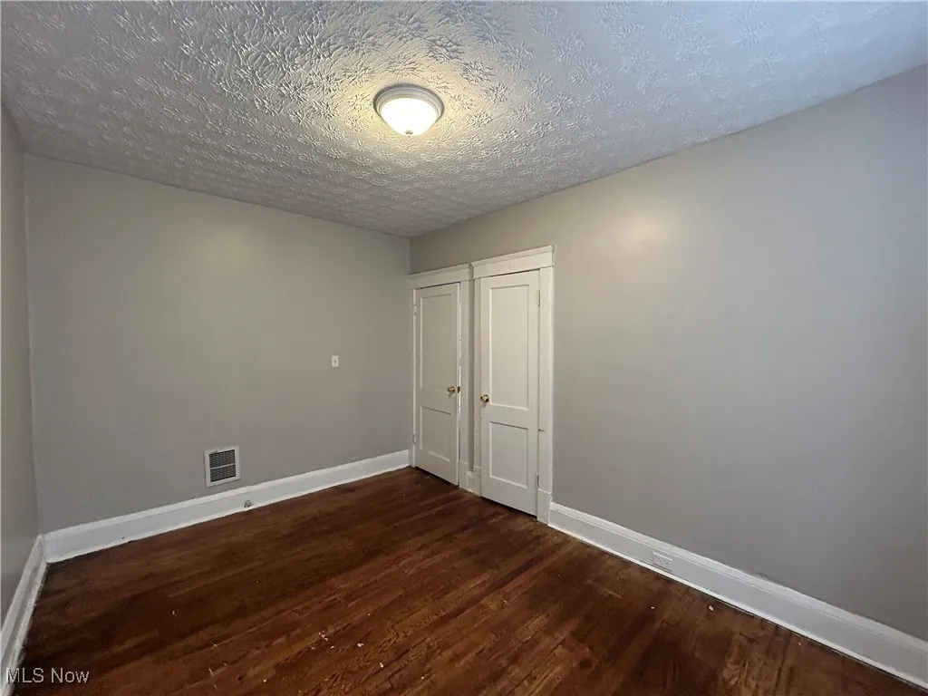Empty room featuring a textured ceiling and dark hardwood / wood-style flooring