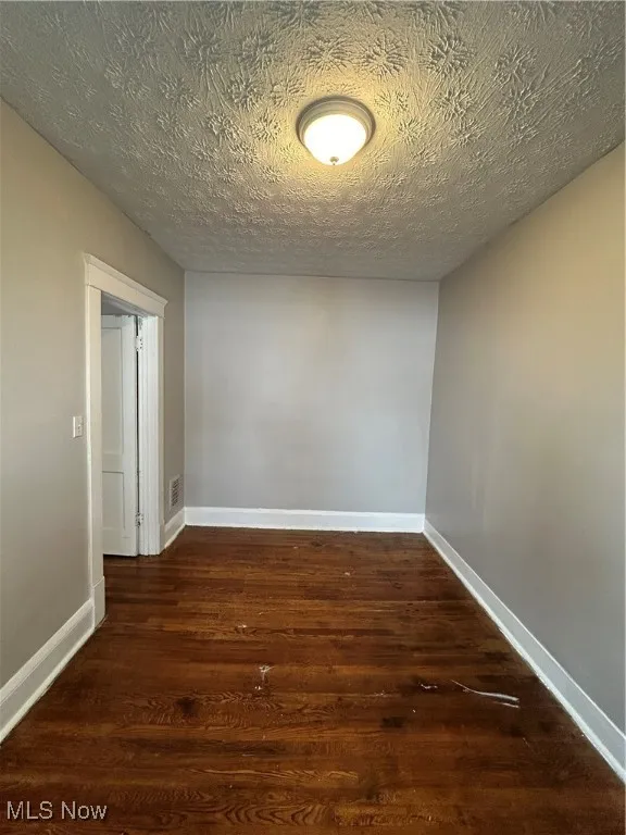 Unfurnished room with a textured ceiling and dark hardwood / wood-style flooring