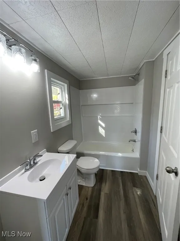 Full bathroom featuring wood-type flooring, a textured ceiling, toilet, vanity, and shower / bathtub combination