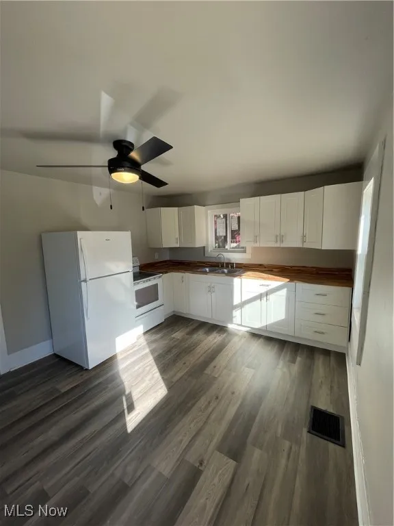 Kitchen with white cabinets, dark hardwood / wood-style flooring, ceiling fan, stove, and refrigerator