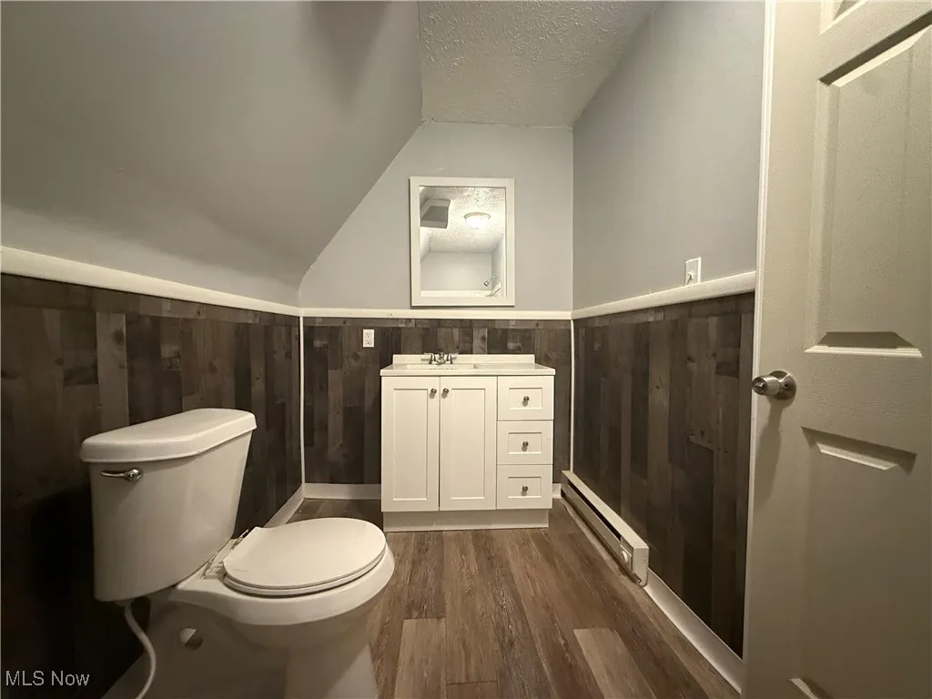 Bathroom with lofted ceiling, a baseboard heating unit, hardwood / wood-style floors, toilet, and vanity