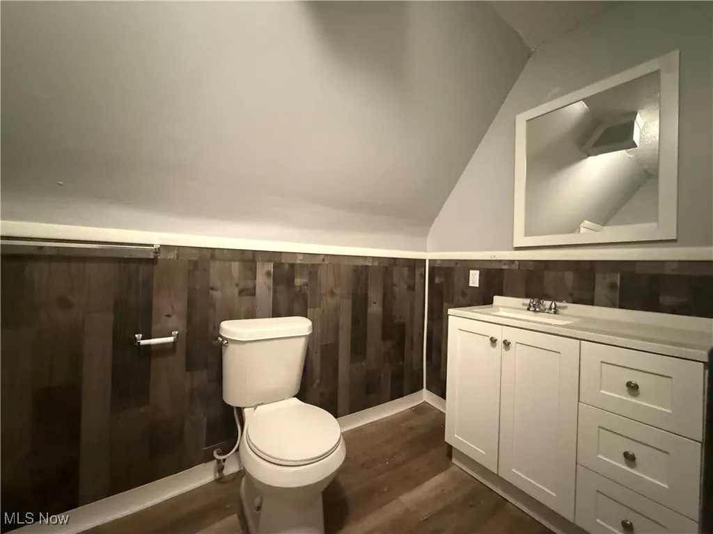 Bathroom with hardwood / wood-style flooring, vaulted ceiling, toilet, wood walls, and vanity