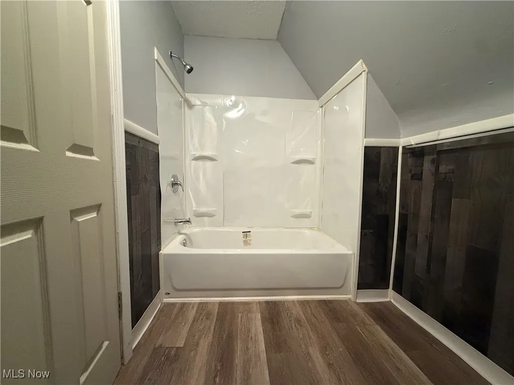 Bathroom featuring shower / bathing tub combination, hardwood / wood-style floors, and vaulted ceiling