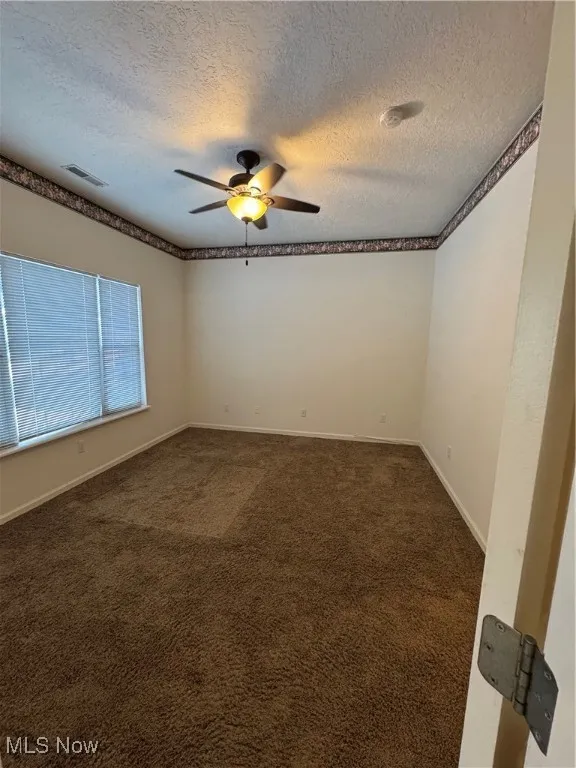 Unfurnished room with ceiling fan, dark carpet, and a textured ceiling