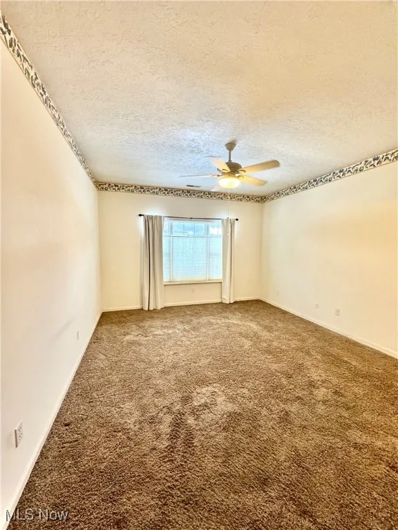 Carpeted spare room with ceiling fan and a textured ceiling