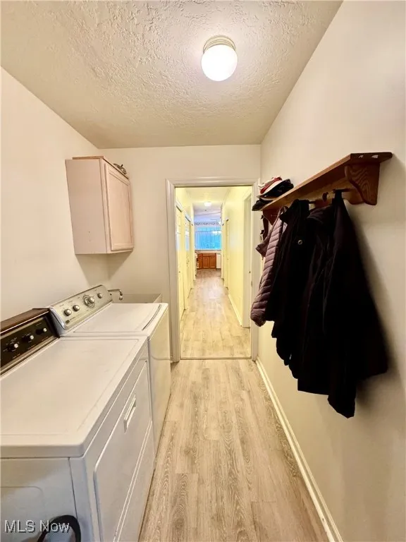 Clothes washing area with cabinets, a textured ceiling, washer and clothes dryer, and light hardwood / wood-style flooring
