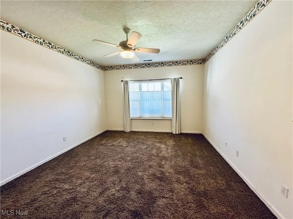 Empty room featuring baseboards, dark colored carpet, ceiling fan, and a textured ceiling
