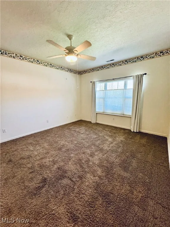Spare room featuring dark carpet, a textured ceiling, visible vents, and a ceiling fan