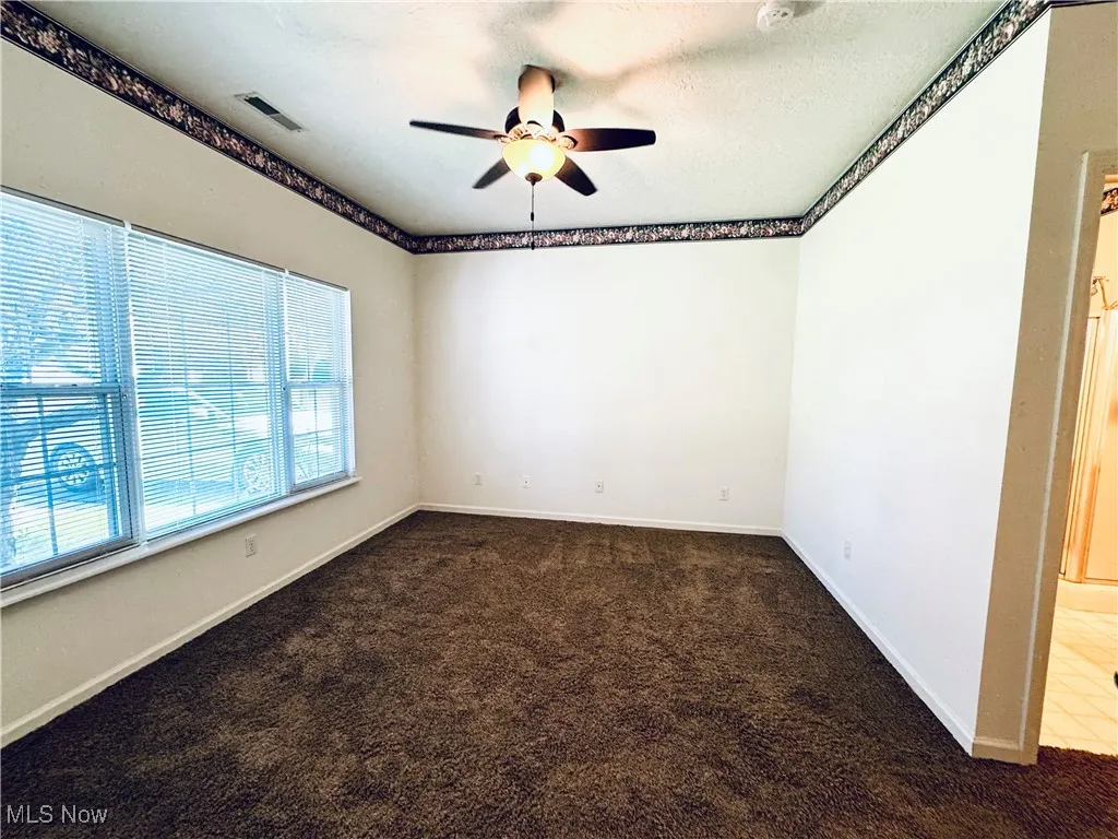Carpeted spare room with ceiling fan, baseboards, and visible vents