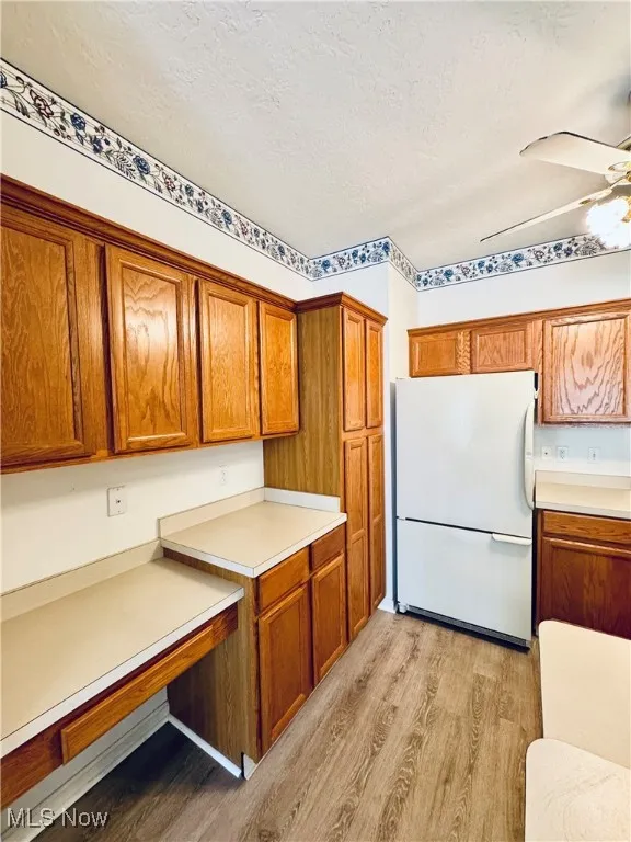 Kitchen with a textured ceiling, light countertops, freestanding refrigerator, light wood-type flooring, and brown cabinetry