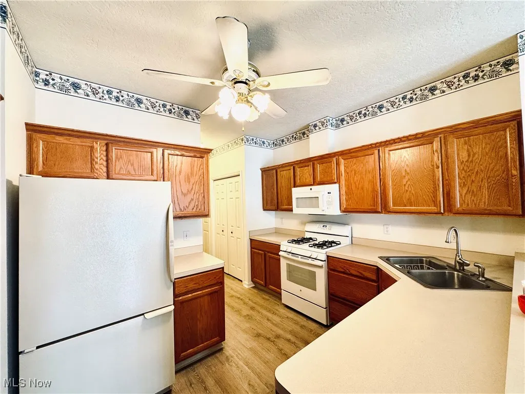 Kitchen featuring a sink, light wood-style floors, white appliances, a ceiling fan, and light countertops