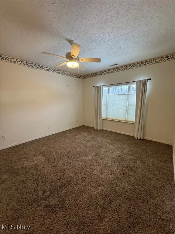 Spare room featuring ceiling fan, a textured ceiling, and dark colored carpet