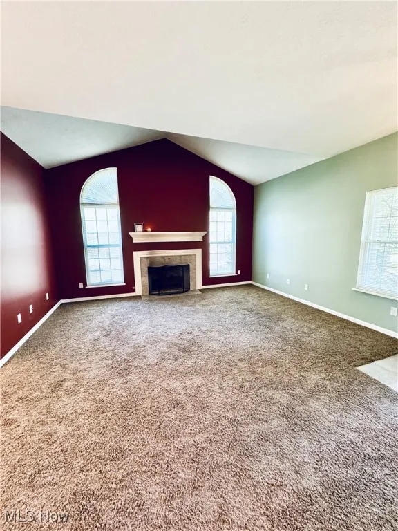 Unfurnished living room featuring carpet flooring, a tiled fireplace, a wealth of natural light, and baseboards