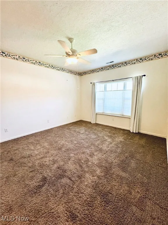 Spare room featuring dark carpet, a ceiling fan, and a textured ceiling