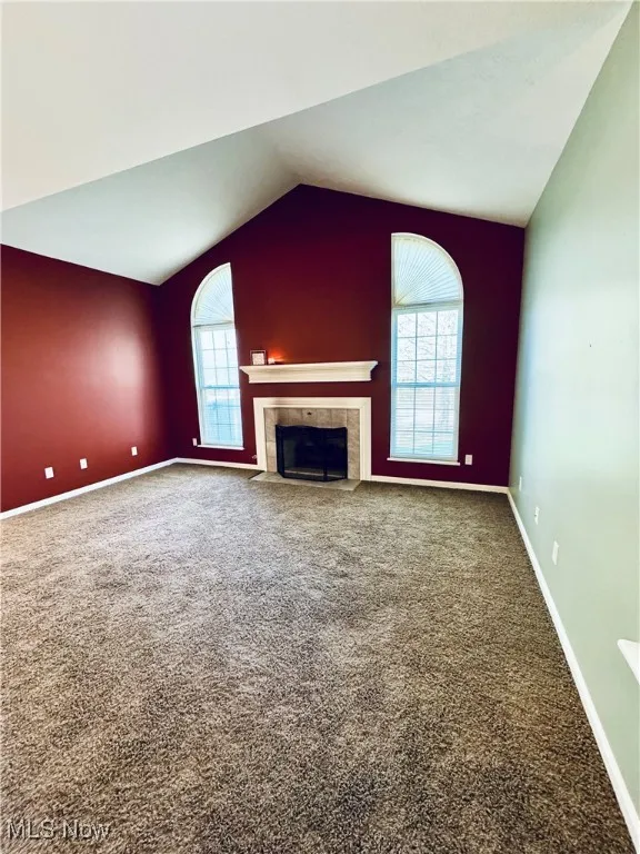 Unfurnished living room with a tile fireplace, carpet flooring, lofted ceiling, and baseboards