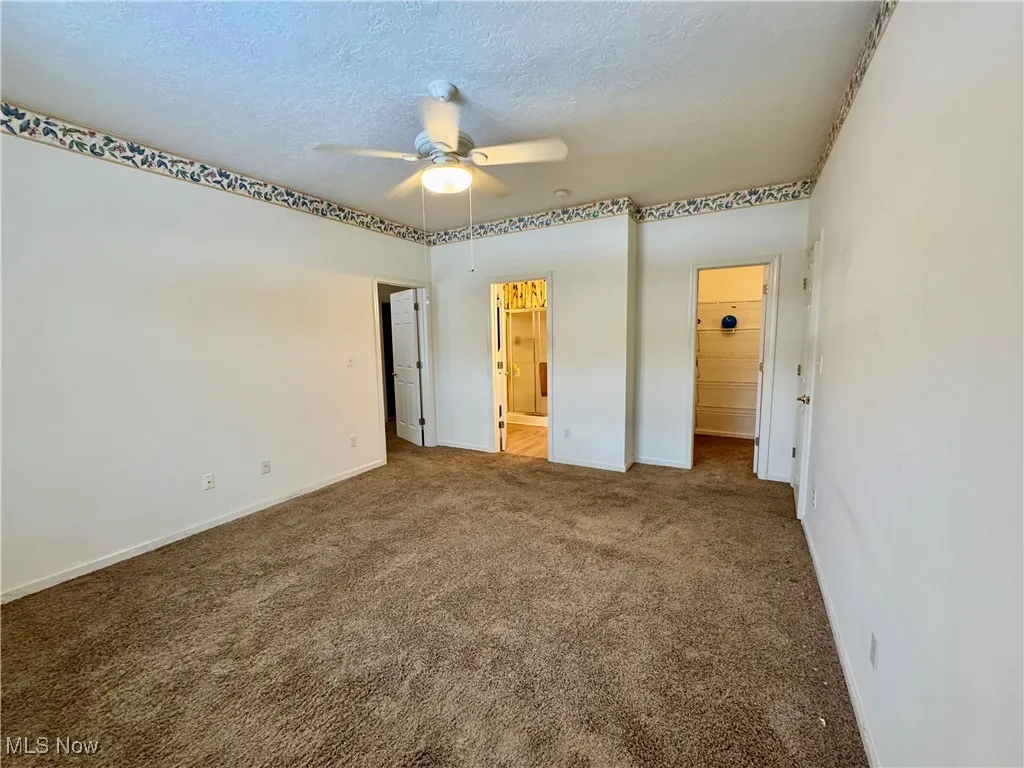 Unfurnished bedroom with a textured ceiling, carpet floors, ceiling fan, and ensuite bathroom