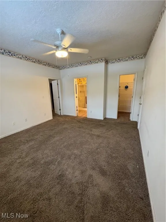 Empty room featuring ceiling fan, a textured ceiling, and dark colored carpet