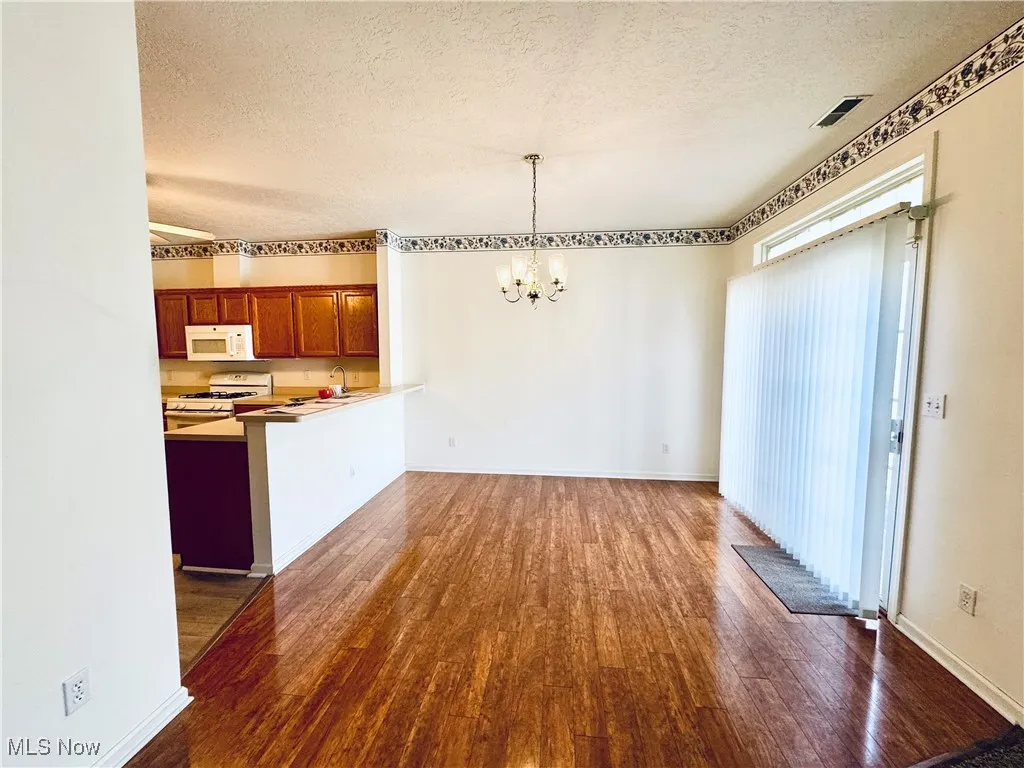 Unfurnished dining area featuring an inviting chandelier, a textured ceiling, wood finished floors, and baseboards