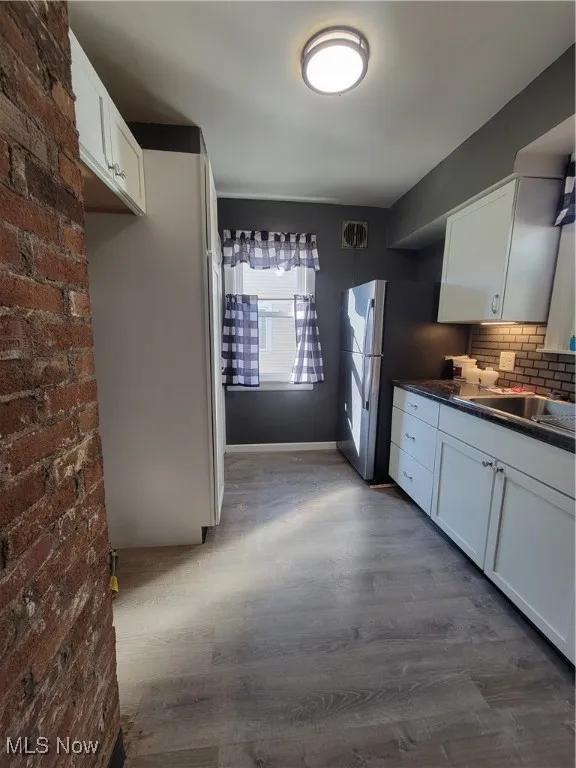 Kitchen with dark hardwood / wood-style flooring, brick wall, backsplash, and white cabinets