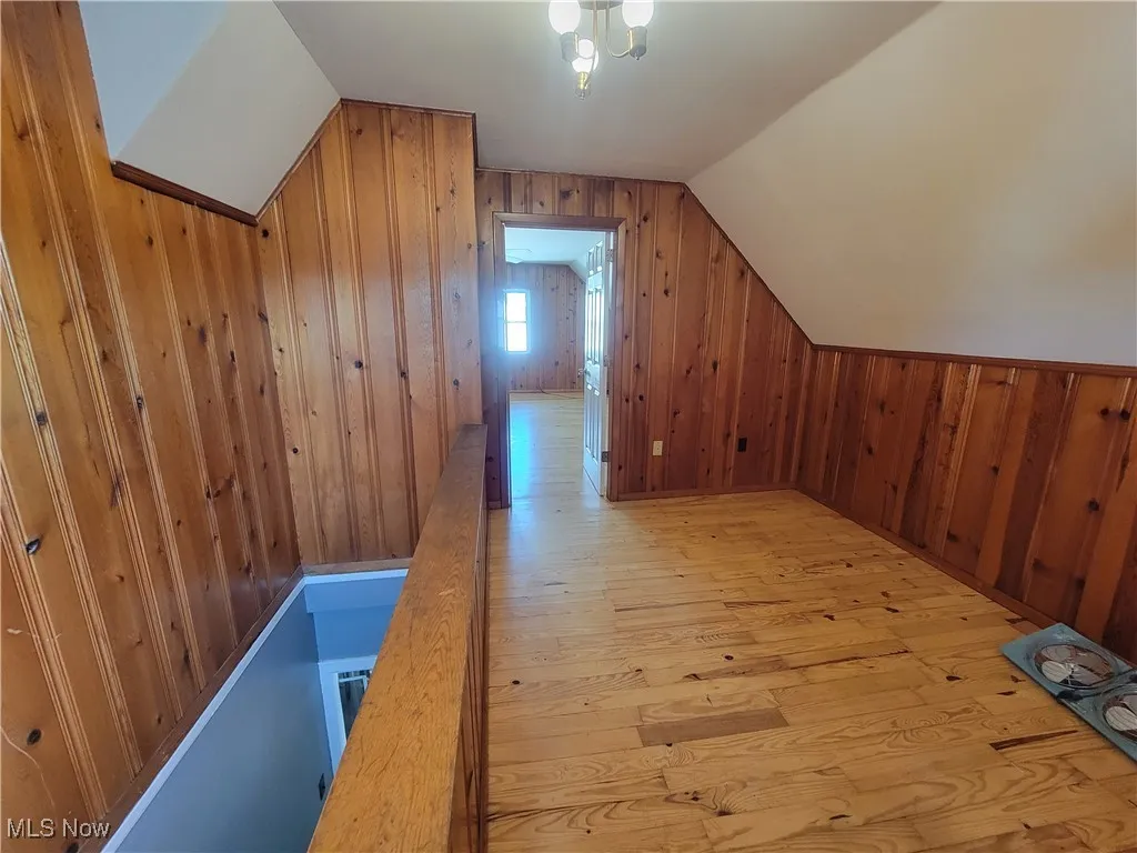 Additional living space with wood walls, light wood-type flooring, and lofted ceiling