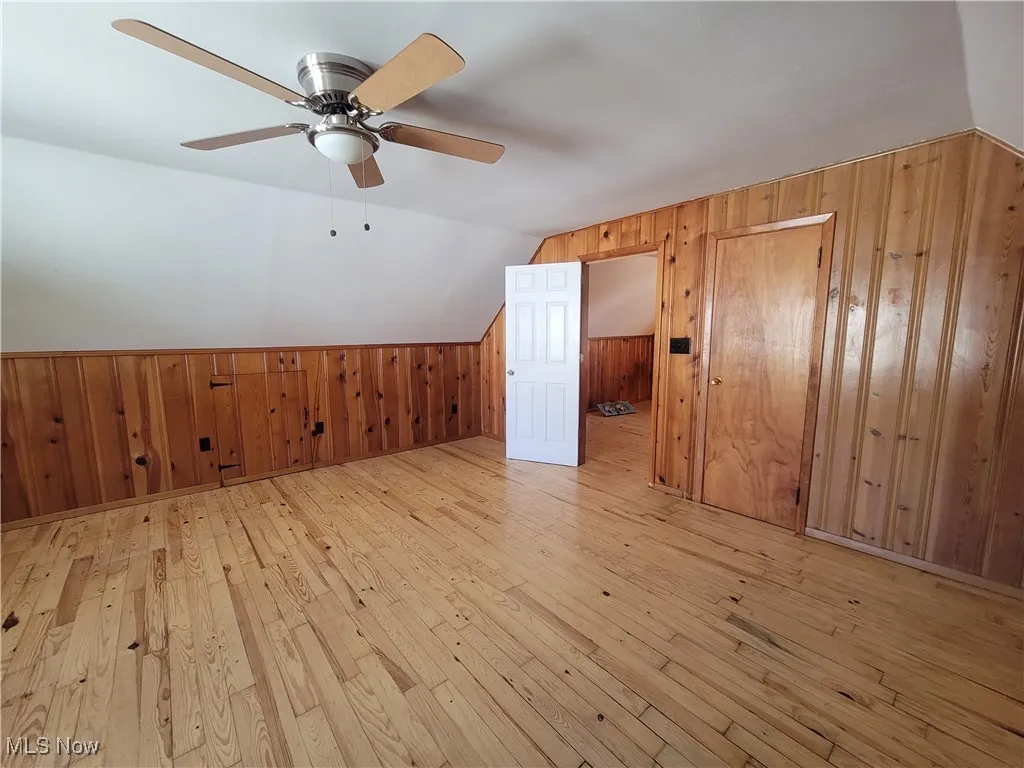 Additional living space with wooden walls, light wood-type flooring, and lofted ceiling