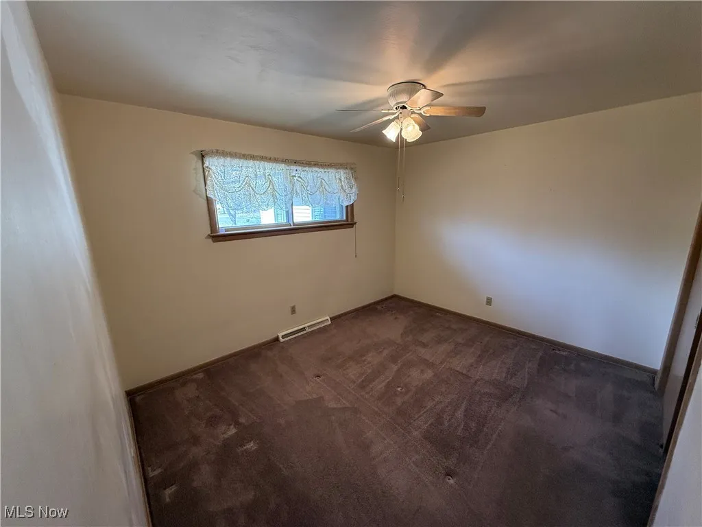 Empty room featuring dark colored carpet and ceiling fan