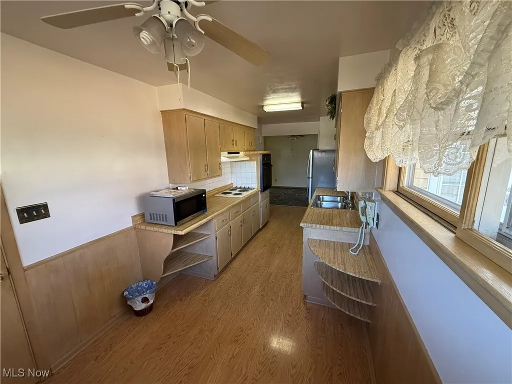 Kitchen with sink, appliances with stainless steel finishes, tasteful backsplash, ceiling fan, and light wood-type flooring