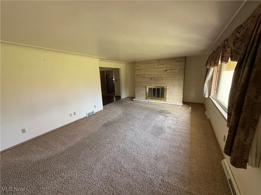 Unfurnished living room with a baseboard heating unit, carpet, and a fireplace